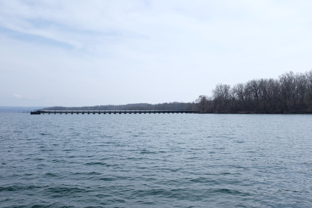 This power plant stopped burning fossil fuels. Then Bitcoin came along. 6 a wide shot of a long metal pipe extending from a woodsy shore into the waters of Seneca Lake